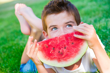Child eating juicy watermelon outdoors on grass