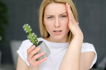 Stressed Exhausted Young Woman Having Strong Tension Headache. Closeup Portrait Of Beautiful Sick Girl Suffering From Head Migraine, Feeling Pressure And Stress. Pain concept with cactus. Soft focus