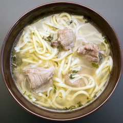 Soup noodles with meat in a plate on a dark background closeup