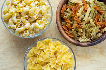 macaroni rigati A wooden white and glass bowl with pasta on a textured wooden rustic table, close-up view from the top.