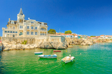 Scenic landscape of abandoned Palace Seixas and boats on the waterfront of Cascais, Lisbon Coast in Portugal. Praia da Rainha on the distance. Turquoise sea in summertime. Copy space with blue sky. - obrazy, fototapety, plakaty