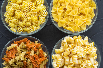 Macaroni ruote Different pasta in a glass bowl with spiral pasta on a textured black background, close-up view from the top.