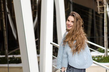 Young attractive lady with long curly hair  wearing stylish clothes is posing in the street, urbanist background
