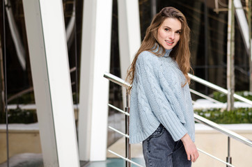 Young attractive lady with long curly hair  wearing stylish clothes is posing in the street, urbanist background