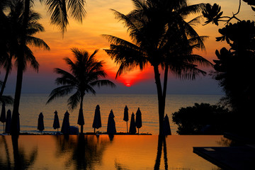 Sun rise at beach front with silhouette coconut or palm tree ,umbrella and pool with reflection