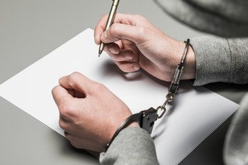 Hands of the criminal in handcuffs write a handle on paper. Sincere confession, request, statement....