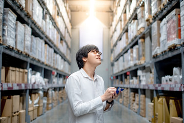 Fototapeta na wymiar Young Asian man standing checking the shopping list and looking for product in warehouse wholesale, shopping warehousing concept