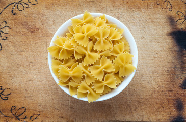 farfalle macaroni pasta in a white cup on a wooden cutting board, textured background, in the center close-up from the top.
