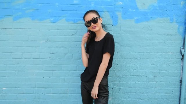 Young beautiful asian girl wearing sunglasses and smiling posing near wall outdoors