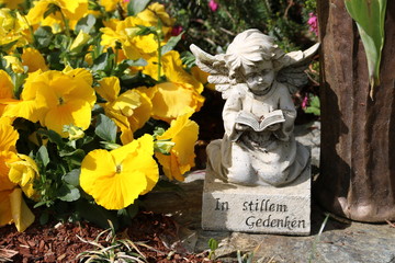 Enge schmückt  ein Grab im Frühling neben Blumen