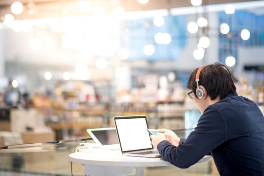 Young Asian business man listening to music by headphones and smartphone while working with laptop computer in co working space. freelance or digital nomad lifestyle in urban workspace concept