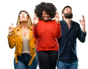 Obraz premium Group of three young men and women with crossed fingers asking for good luck