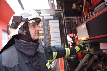 Obraz premium Feuerwehrmann bedient Technik am Löschfahrzeug zur Bekämpfung von Hausbränden // Firefighter operates technology on fire engine to fight house fires
