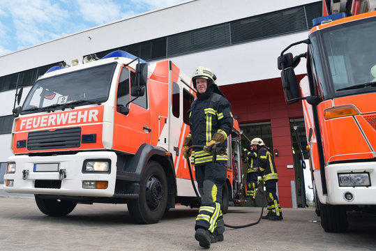 Feuwehrwehr: Feuerwehrmänner am Löschfahrzeug vor dem Einsatz zur Bekämpfung eines Brandes an der Feuerwache // Fire brigade: firefighters at the fire station