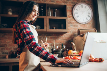 Female cook in apron looks at a recipe in laptop