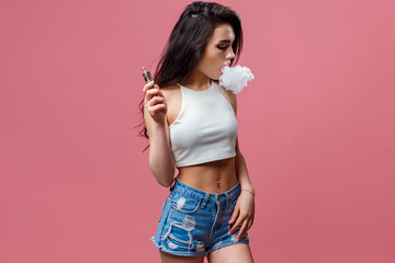 Casual pretty woman standing and vaping on pink background in studio.