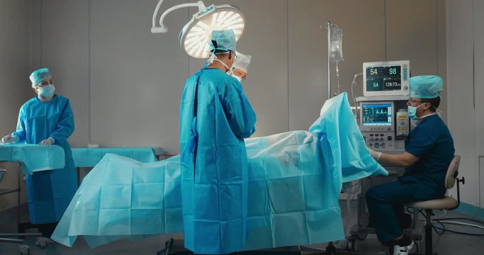 Medical team, doctors performing surgical operation in real modern operating theater. 4K UHD 60 FPS SLO MO