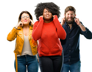 Group of three young men and women covering ears ignoring annoying loud noise, plugs ears to avoid hearing sound. Noisy music is a problem.