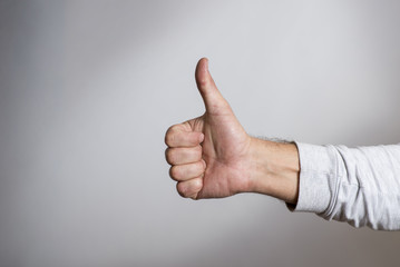 Hand with thumb upwards on a gray background. Man hand giving thumbs up