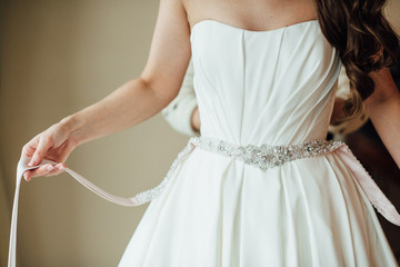 Bride holds in hands a pink satin belt with diamonds on a white wedding dress