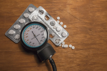 Sphygmomanometer with white medicine drugs on a wooden surface.