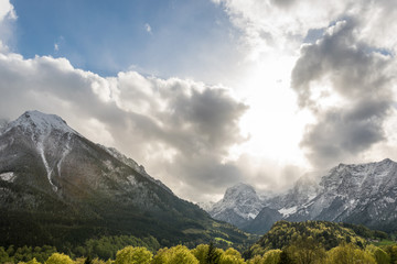 Fototapeta premium Die Sonne scheint durch die Wolken auf Berge im Frühling