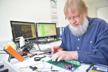 Ingenieur in der Entwicklung von Elektronik am Arbeitsplatz - Portrait älterer Physiker in einer...