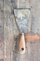 Old, dirty putty knife against wooden plank. Tool series.