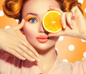 Beauty joyful teenage girl takes juicy oranges. Teen model girl with freckles, funny red hairstyle, yellow makeup and nails on polka dots background
