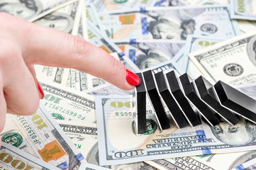Female hand stopping domino effect on dollar backgrounds. Business concept.