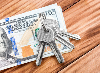 Keys with stack of dollar bills on wooden table. Top view.