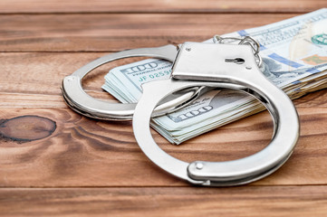 Handcuffs with heap of money on the wooden table.