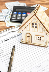 Property assessment form with money, calculator and model of house on the table. Property valuation concept.