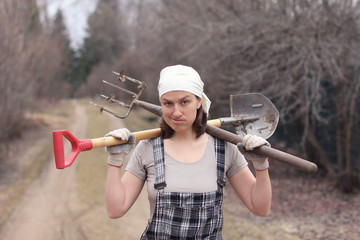 Gardener/farmer woman with spade and pitchfork on her shoulders. Tired after work.