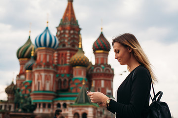 Girl travels in Moscow. She walks in the Red Squere. Young woman looks into cell phone. Near old russian church.