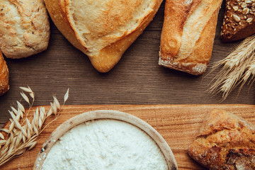 Naklejka premium Fresh fragrant bread on the wooden table with cutting board and flour. Food concept
