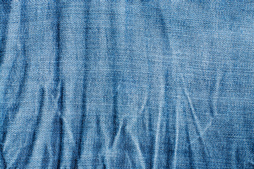 Texture of blue wrinkled faded jeans textile closeup