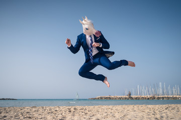 Stylish manager in funny mask and elegant suit jumps on beach