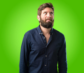 Young hipster man with big beard doubt expression, confuse and wonder concept, uncertain future over green background