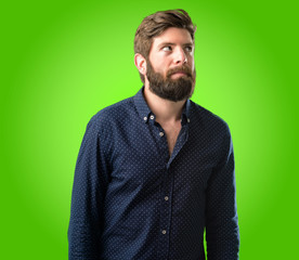 Obraz premium Young hipster man with big beard doubt expression, confuse and wonder concept, uncertain future over green background