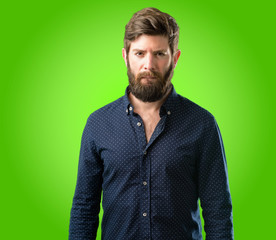 Young hipster man with big beard doubt expression, confuse and wonder concept, uncertain future over green background