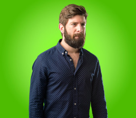 Fototapeta premium Young hipster man with big beard doubt expression, confuse and wonder concept, uncertain future over green background