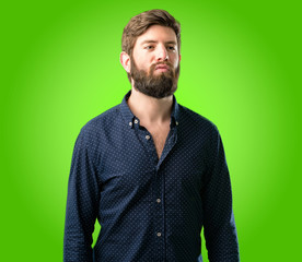 Obraz premium Young hipster man with big beard expressing love, blows kiss at camera, flirting over green background