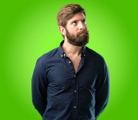 Young hipster man with big beard doubt expression, confuse and wonder concept, uncertain future over green background