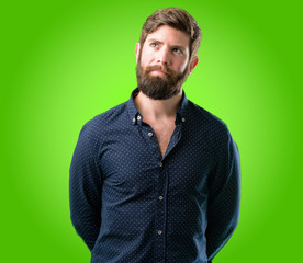 Young hipster man with big beard doubt expression, confuse and wonder concept, uncertain future over green background