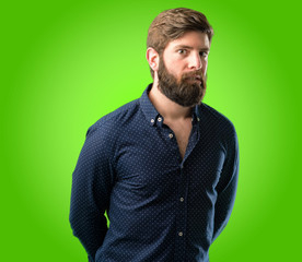 Fototapeta premium Young hipster man with big beard doubt expression, confuse and wonder concept, uncertain future over green background