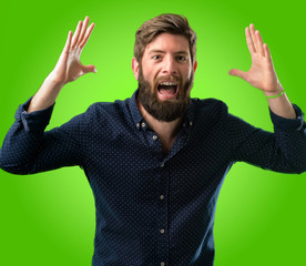 Young hipster man with big beard happy and surprised cheering expressing wow gesture over green background