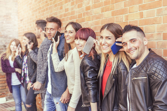 Large Group Of Friends Using Smart Phone Against A Red Wall