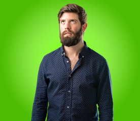 Young hipster man with big beard making funny face fooling over green background