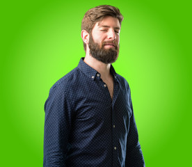 Young hipster man with big beard blinking eyes with happy gesture over green background